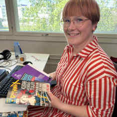 Mediatutkija Laura Antola pitelee väitöskirjansa versiota ja sarjakuvalehtiä käsissään työhuoneessaan Turun yliopistolla.
