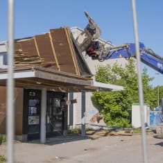 En rivningsmaskin river ett entrétak till en gammal skolbyggnad.