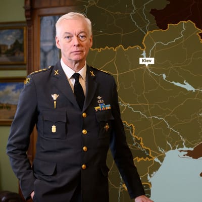 Militärexperten Joakim Paasikivi står i ett rum och en grafiska karta av Ukraina med den ryska krigsfronten har blivit editerad in i bilden bakom Paasikivi.