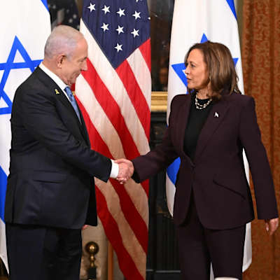 Israels premiärminister Benjamin Netanyahu skakar hand med USA:s vicepresident Kamala Harris. Amerikanska och israeliska flaggor syns i bakgrunden.