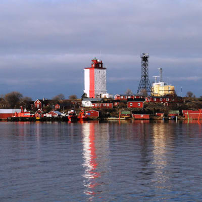 Utsikt från havet över Utö, där den rödvita fyren speglas i vattnet.