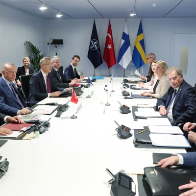 Folk vid ett långbord. I bakgrunden syns Natos, Turkiets, Finlands och Sveriges flagga.