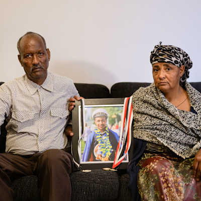 Ghidey Embaye Tela och Hadas Kibrom Woldemariam sitter i en soffa med studentfotot på sin avlidna son mellan dem. 