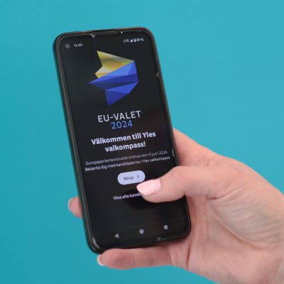 En hand som håller i en smarttelefon med Yles valkompass.