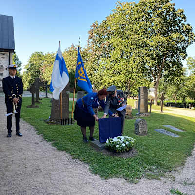 En kvinna i scoutuniform och en man i militär paraduniform avtäcker en minnestavla på en kyrkogård.