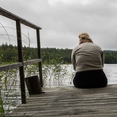 En kvinna sitter på ändan av en brygga en mulen dag. 