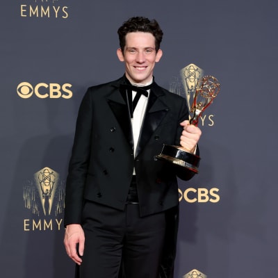Josh O'Connor, klädd i svart kostym och vit skjorta, poserar med sin Emmystatyett framför en svart vägg. Han ler och tittar in i kameran.