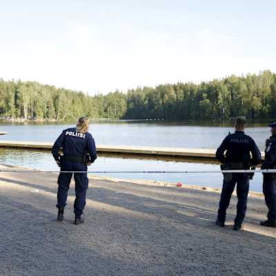 Tre poliser vid Hanaböle träsk i Vanda. Poliserna har ryggarna vända mot kameran och tittar mot vattnet.