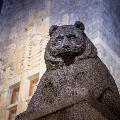 Stenbjörnen framför Nationalmuseet i Helsingfors i kvällsbelysning. I bakgrunden syns museibyggnaden.