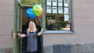 Kvinna står i dörröppning med ballonger i handen.