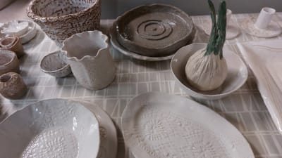 Keramikkärl i grått, vitt och brunt. I en vit skål står en lök gjord av keramik.