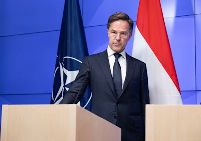 Mark Rutte vid ett talarpodium framför en Natos och Nederländernas flaggor.