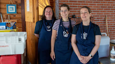 Tre kvinnor med blåa förkläden och scouthalsdukar.