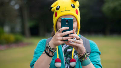 En person med en gul mössa föreställande pokemonen pikachu. Personen håller en telefon framför ansiktet.