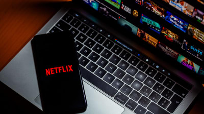 En laptop där Netflix hemskärm syns på skärmen samt en mobiltelefon där man ser Netflix logo.