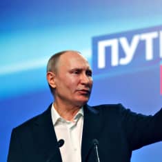 Vladimir Putin pitää puhetta ja osoittaa vasemman kätensä etusormella jotakin.