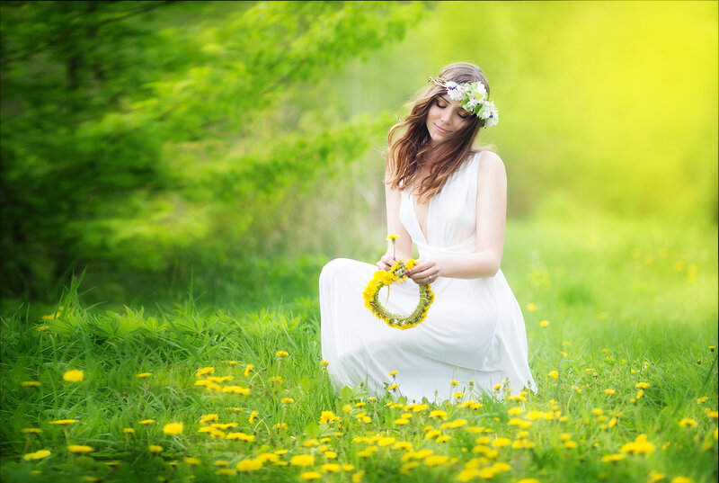 Image of pretty woman in a white dress weaves garland from dandelions in the field, happy  cheerful girl resting on dandelions meadow, relaxation outdoor in springtime, vacation.