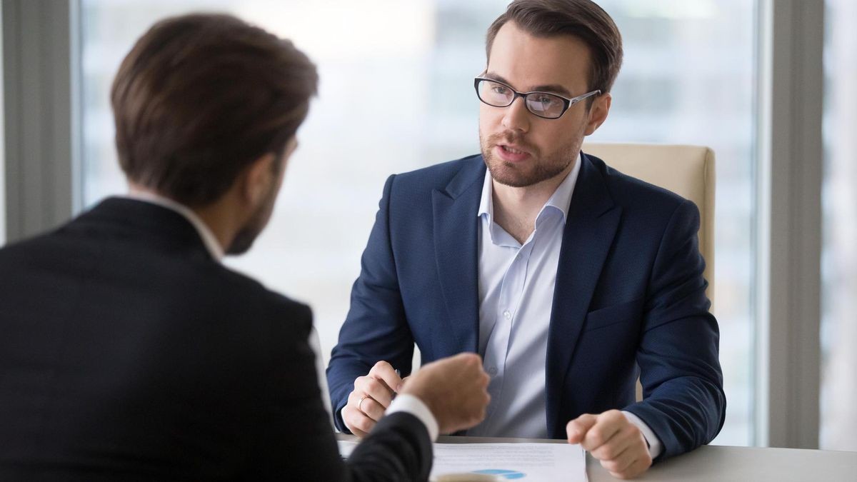 Focused male business partners negotiate at office table discussing statistics, male managers talk about sales and contract terms, businessmen consider deal closing, speak about success strategies