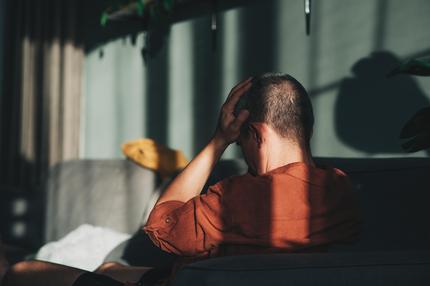 Long Covid: Unpleasant pain. Sad unhappy handsome man sitting on the sofa and holding his forehead while having headache