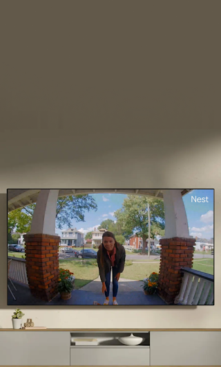 A TV in a living room showing a delivery person standing on a stoop waving to the doorbell camera.