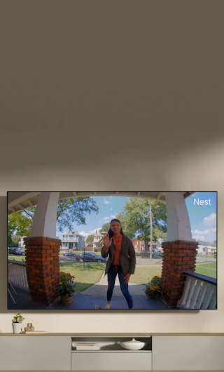 A TV in a living room showing a delivery person standing on a stoop waving to the doorbell camera.