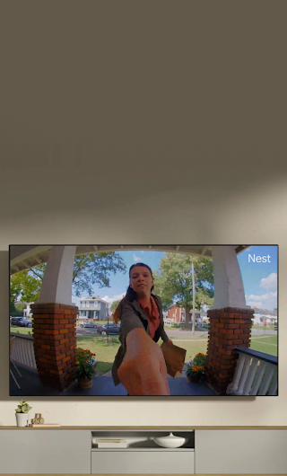 A TV in a living room showing a delivery person standing on a stoop waving to the doorbell camera.