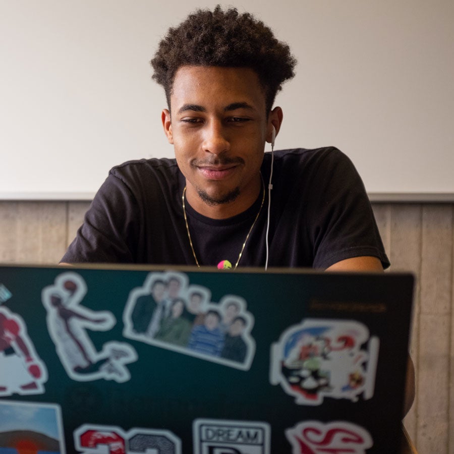 Male student in front a laptop with stickers on the cover