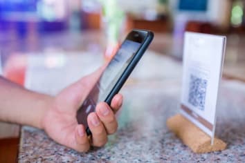 A hand with a smartphone scanning a QR code on a business counter