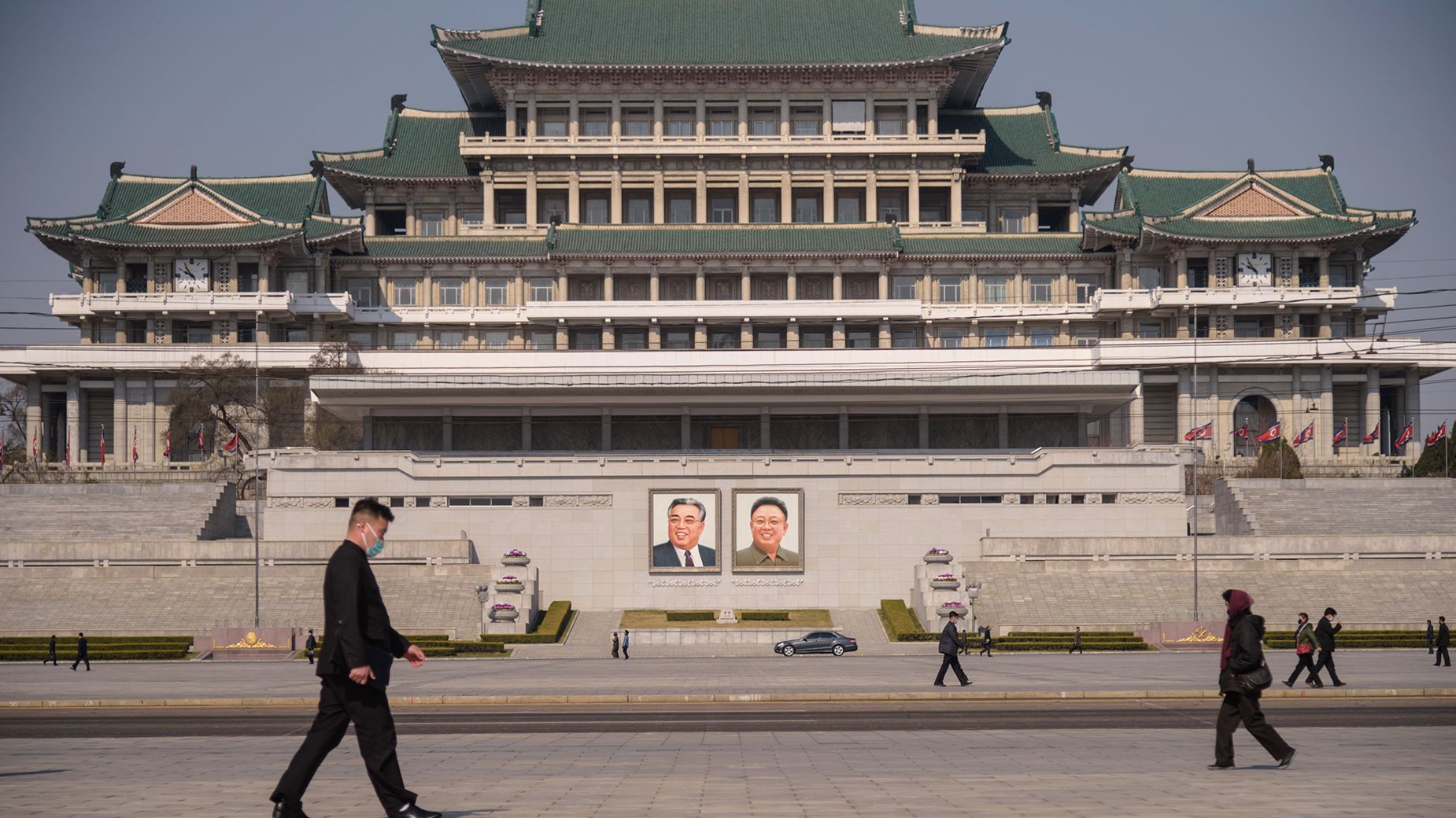 People wearing face masks walk before the portraits of late North Korean leaders Kim Il Sung and Kim Jong Il (centre R) on Kim Il Sung Square in Pyongyang on April 9, 2020. (Photo by KIM Won Jin / AFP) (Photo by KIM WON JIN/AFP via Getty Images)