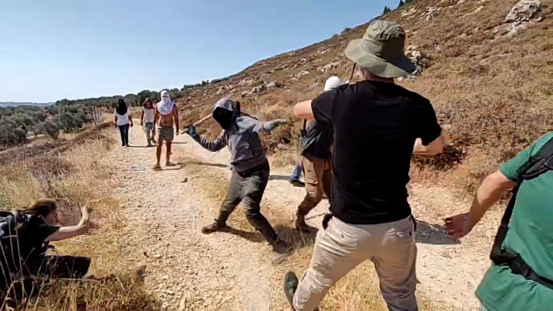 Masked Israeli settlers and Palestinian farmers and foreign activists clash in the West Bank town of Qusra on Sunday, in this screengrab made from a video obtained by CNN.