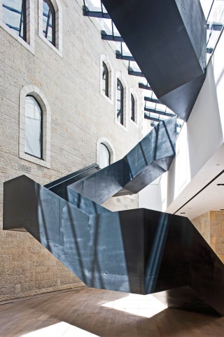 Charcoalhued steel sheets ascend through the open atrium at the Mamilla Hotel in Jerusalem against a backdrop of local...