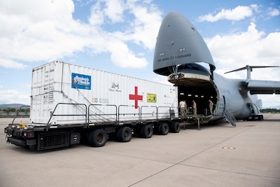 Airmen move a large container from the open cargo bay of a C-5B transport jet to a trailer on the tarmac.