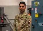 A man poses for a photo in a maintenance shop with a saw table behind him.