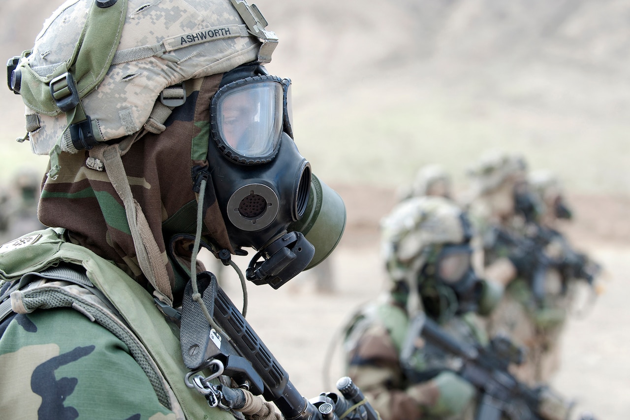Uniformed service members are shown wearing protective gear including gas masks.