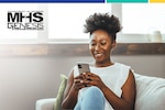 Woman sits on couch and smiles while looking down at smartphone.