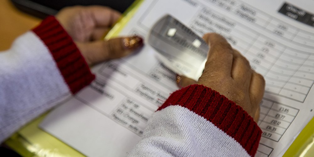 Close up of a person's hands using a magnifier on a sheet a paper.