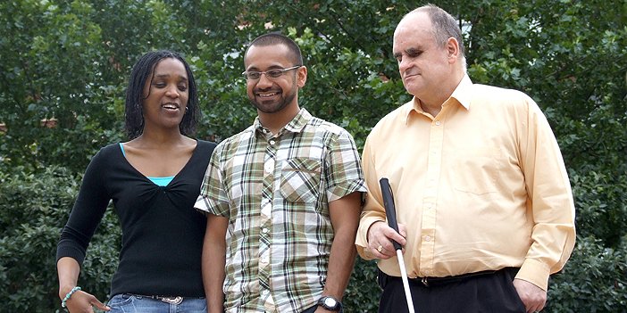 A group of three blind or partially sighted adults, one holding a white cane. These are the people who will benefit from RNIB volunteer support.