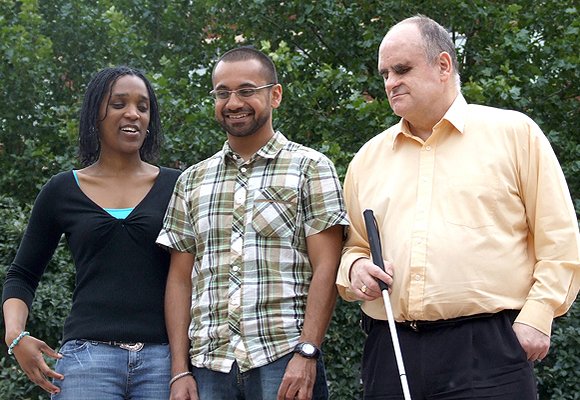 A group of three blind or partially sighted adults, one holding a white cane. These are the people who will benefit from RNIB volunteer support.