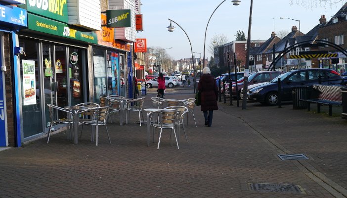 Outdoor café furniture partially blocking a wide footpath.