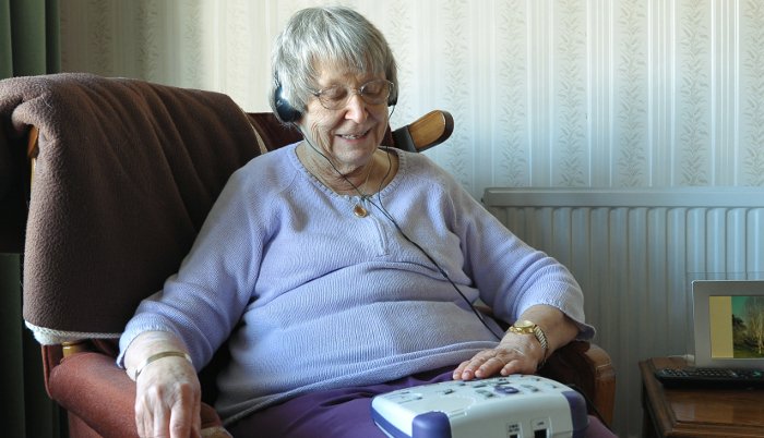 A woman sits in a chair and listens to a talking book.