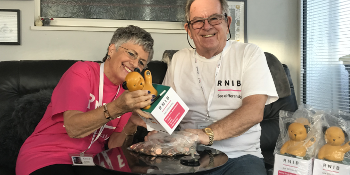 RNIB volunteers Alan and Janet on a sofa, smiling and counting donations from Sooty Boxes.