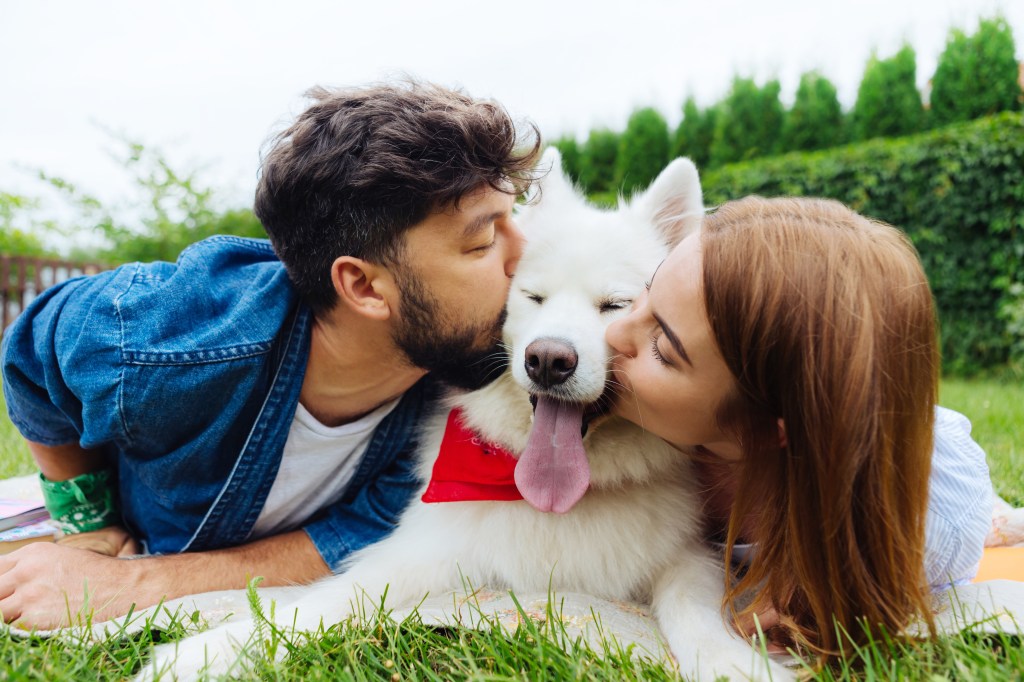 A bearded man and his girlfriend affectionately kissing their dog during a weekend getaway
