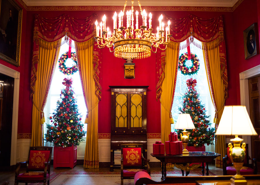 Resting atop a table, cranberries create gift boxes in festive celebration, and placed in planter boxes, two pine trees dressed in ornaments stand in the window frames.