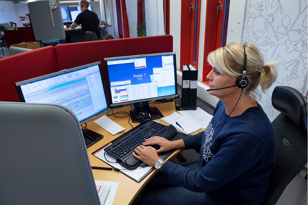 Person sitter med hörlurar och två stora skärmar vid ett skrivbord.