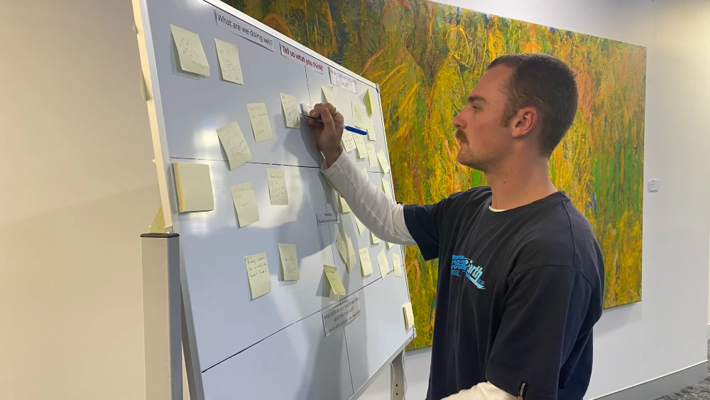 A student contributing feedback by writing on a post-it note on a whiteboard