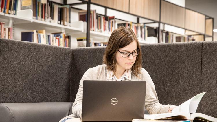 Student sitting in Library with a laptop and book on table