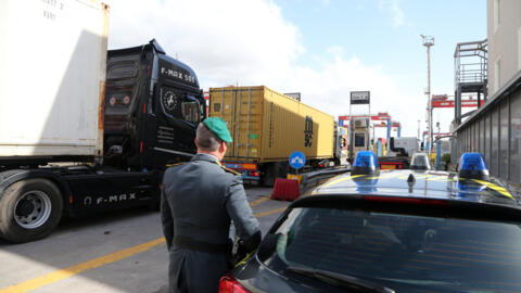 صورة توضيحية لأحد أفراد الشرطة الإيطالية المسؤولة عن الجرائم المالية والتهريب، يراقب الشاحنات في المنطقة التجارية بميناء نابولي، 29 فبراير/شباط 2024.