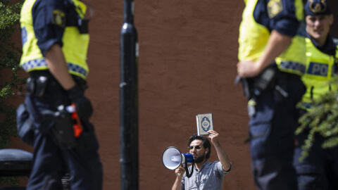 عناصر من الشرطة السويدية أمام لاجئ عراقي بصدد إحراق القرآن، 28 يونيو/حزيران 2023. 