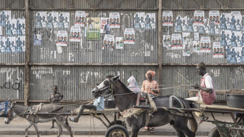 Carts ride past electoral posters in Dhara on March 21, 2024, as eighteen men and one woman are in the running for the March 24 vote to become Senegal's fifth president.