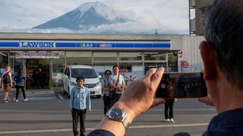 This photo taken on May 20, 2024 shows tourists taking pictures of Mount Fuji from opposite a convenience store in the town of Fujikawaguchiko, Yamanashi prefecture.